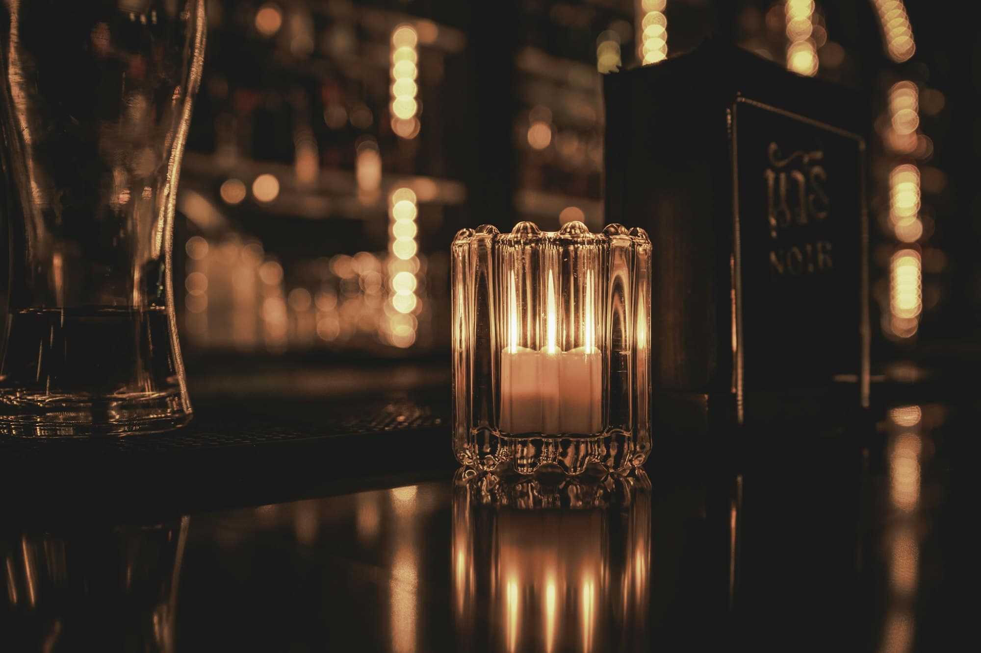 A lit candle in a ribbed glass holder on a bar counter at night